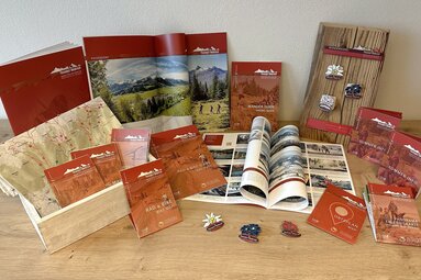 Brochures, hiking and cycling maps, and pins from Piesendorf and Niedernsill are displayed on a wooden table. | © TVB Piesendorf Niedernsill