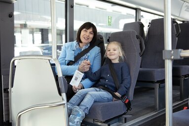 Erwachsene Person und Kind sitzen angeschnallt im Bus und zeigen ein Guest Mobility Ticket mit QR-Code. | © Salzburger Verkehrsverbund