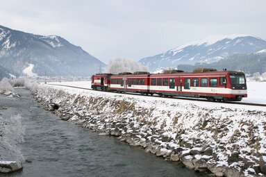 Pinzgauer Lokalbahn travels beside a river through a snow-covered Alpine valley in winter. | © MeinBezirk.at