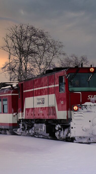 Pinzgauer Lokalbahn travels through a snowy winter landscape with the sun low in the sky. | © Florian Knapp