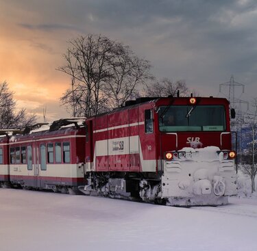 Pinzgauer Lokalbahn travels through a snowy winter landscape with the sun low in the sky. | © Florian Knapp