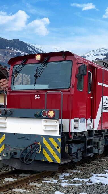 Red and white Pinzgauer Lokalbahn at Niedernsill station, with partly snow-covered mountain slopes behind. | © Florian Knapp