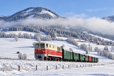 Nostalgiezug der Pinzgauer Lokalbahn mit rot-cremefarbener Lokomotive fährt durch eine verschneite Landschaft im Pinzgau. | © KI generiertes Bild