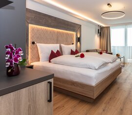 Zimmer im Klawunn Hotel & Apartment mit Doppelbett, Sitzbereich, Schreibtisch, großen Fenstern und roten Akzenten. | © nikolaus faistauer photography