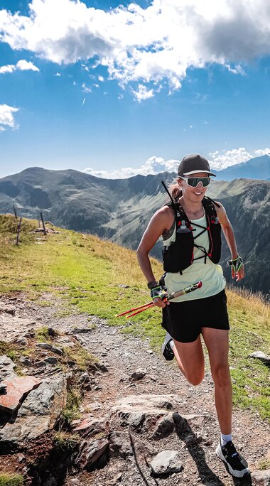 rail runner passes a wooden cross on a mountain trail, with an alpine mountain landscape in the background. | © SalzburgerLand Tourismus © Foto Philipp Freund