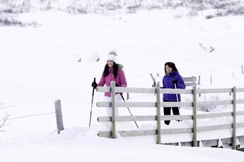 Two people snowshoeing with poles beside a wooden fence in the snow-covered Rauris Valley. | © NPHT, Floria Bachmeier - Raurisertal