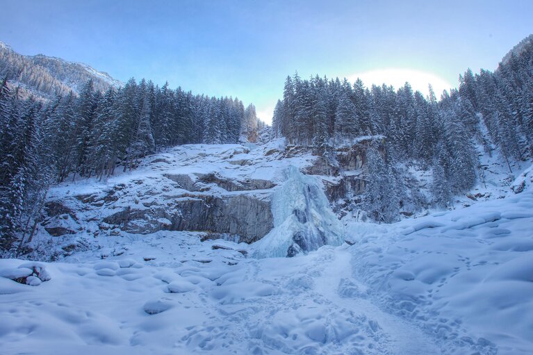 Partly frozen Krimml Waterfalls surrounded by snow-covered rocks and coniferous forest in winter. | © Zillertal Arena
