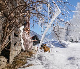 Person mit Holzschlitten an einer Hütte, umgeben von Schnee, Eiszapfen und bereiften Bäumen unter blauem Himmel. | © TVB Piesendorf Niedernsill, Foto Harry Liebmann