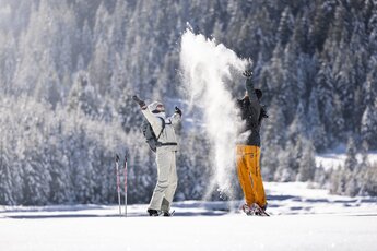 Zwei Personen mit Schneeschuhen werfen in einer verschneiten Berglandschaft Schnee in die Luft. | © Ferienregion Nationalpark Hohe Tauern, Foto Daniel Breuer
