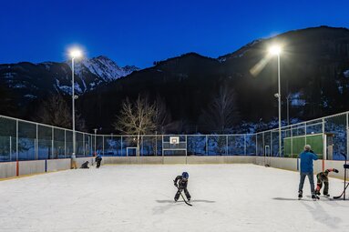 Kinder und Erwachsene beim Eislaufen und Eishockey auf dem beleuchteten Eislaufplatz in Niedernsill. | © Lichtfarben