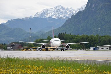 Passenger aircraft at Salzburg Airport with forested mountains and snow-covered peaks in the background. | © Stabstelle Presse, Flughafen Salzburg