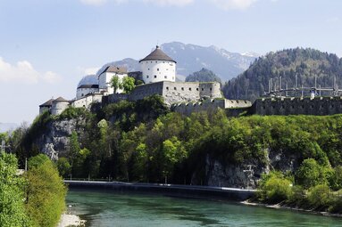 Kufstein Fortress on a wooded rock above the Inn River, with fortress walls, a round tower and mountains in the background. | © Tirol Werbung, Foto Aichner Bernhard Kufstein