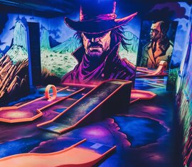 Indoor mini golf course with several lanes, colourful lighting and large Western-style comic illustrations. | © Wildpark Ferleiten 