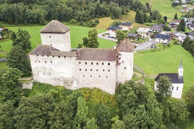 Aerial view of Kaprun Castle with towers and a small church, surrounded by trees, meadows and houses. | © Arne Mueseler - arne-mueseler.com