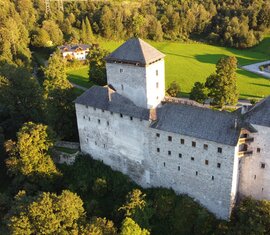 Burg Kaprun aus der Vogelperspektive mit steinernen Mauern und Türmen, umgeben von Wiesen, Bäumen und Gebäuden. | © Burg Kaprun