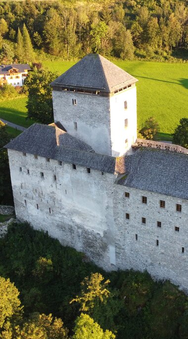 Burg Kaprun aus der Vogelperspektive mit steinernen Mauern und Türmen, umgeben von Wiesen, Bäumen und Gebäuden. | © Burg Kaprun