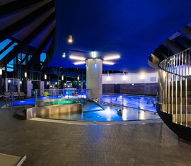 Indoor area of Kristallbad Wald with illuminated pools, loungers, large windows and a spiral staircase. | © Kristallbad Wald Königsleiten GmbH