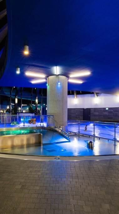 Indoor area of Kristallbad Wald with illuminated pools, loungers, large windows and a spiral staircase. | © Kristallbad Wald Königsleiten GmbH
