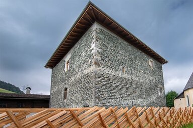 Felberturm with massive stone walls and a wooden fence, with Felberkirche and its tall steeple to the right. | © Foto Franz Reifmüller