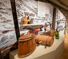 Exhibition room at the Felberturm Museum with historic wooden containers, glass bottles, display panels and a digital media station. | © Foto Franz Reifmüller