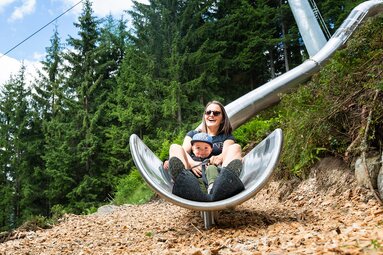 Adult and child on the Wildkogel-Arena slide trail, with a gondola lift and forest beside them. | © Wildkogel Arena Neukirchen & Bramberg