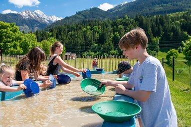 Kinder und Jugendliche waschen im Edelsteinpark Sand mit Schürftellern an einem Wasserbecken. | © Edith Danzer