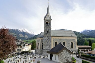 Niedernsill parish church with its stone steeple and cemetery, set against wooded and partly snow-covered mountains. | © TVB Piesendorf Niedernsill, Foto Harry Liebmann