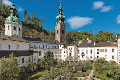 St. Peter's Abbey in Salzburg with church tower, dome and buildings surrounding a green courtyard. | © Erzabtei St. Peter