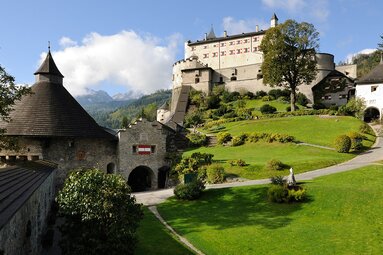 Hohenwerfen Castle with towers and historic buildings, paths, lawns and trees, with wooded mountain slopes behind. | © Salzburger Burgen & Schlösser