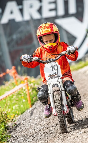Kind mit Helm und Protektoren fährt im E-Motocross Park auf einer Schotterstrecke beim AreitXpress. | © Schmittenhöhebahn AG