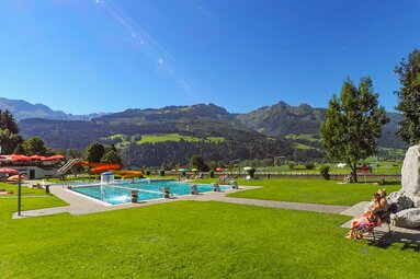 Hinkelsteinbad Piesendorf mit Schwimmbecken, Wasserrutsche und Liegewiese vor grüner Berglandschaft. | © Gemeinde Piesendorf, Foto Lichtfarben