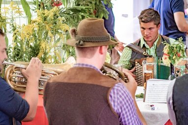 Musiker spielen beim Bartlmä Fest gemeinsam Ziehharmonika und Blechblasinstrumente an einem Tisch. | © Lichtfarben