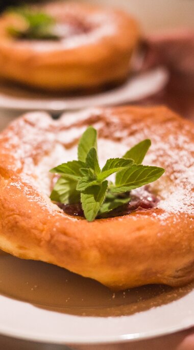 Bauernkrapfen with powdered sugar, fruit filling and mint on a white plate. | © SalzburgerLand Tourismus