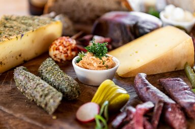 Brettljause mit verschiedenen Käsesorten, Wurst, Speck, Aufstrich, Essiggurken und Radieschen auf einem Holzbrett. | © SalzburgerLand Tourismus