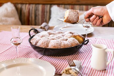 Buchteln dusted with powdered sugar in a pan, with one Buchtel being lifted out using serving utensils. | © SalzburgerLand Tourismus