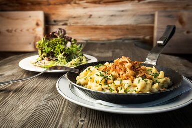 Kasnockn topped with fried onions and chives in a pan, with a plate of green salad in the background. | © SalzburgerLand Tourismus