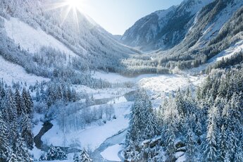 Snow-covered Obersulzbach Valley with coniferous forests, mountain slopes and a stream winding through the valley. | © Ferienregion Nationalpark Hohe Tauern, Foto Daniel Breuer