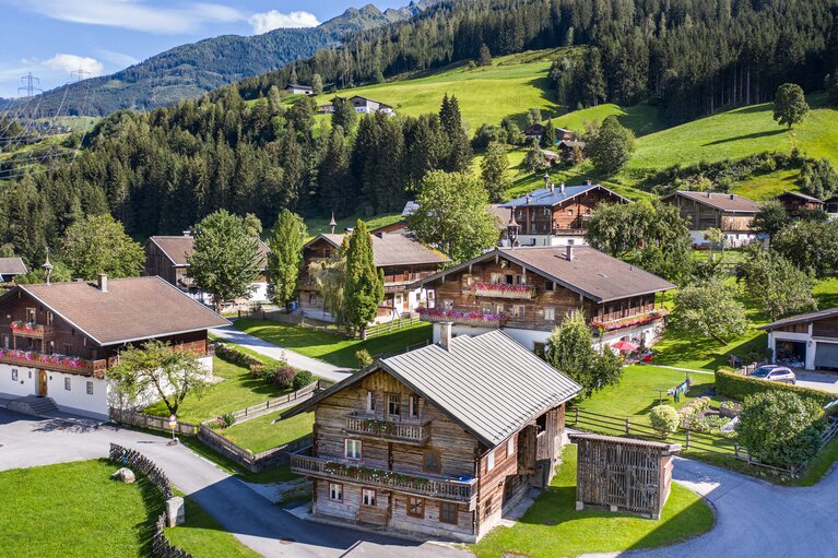 Blick auf Aisdorf bei Niedernsill mit traditionellen Holzhäusern, Wiesen und bewaldeten Berghängen. | © TVB Piesendorf Niedernsill, Foto Harry Liebmann 