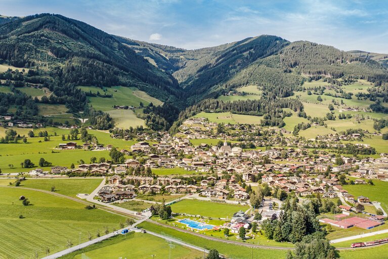Luftaufnahme von Piesendorf mit Ortszentrum, Wiesen und bewaldeten Berghängen im Hintergrund. | © TVB Piesendorf Niedernsill, Foto Harry Liebmann 