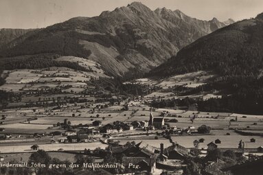 Historische Ansicht von Niedernsill mit Kirche, Häusern und Feldern vor den bewaldeten Berghängen des Mühlbachtals. | © TVB Piesendorf Niedernsill