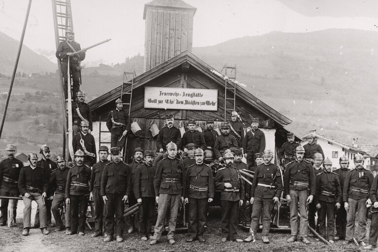 Historische Feuerwehrmannschaft vor einer Feuerwehr-Zeugstätte mit Uniformen, Helmen, Leitern und Löschausrüstung. | © TVB Piesendorf Niedernsill