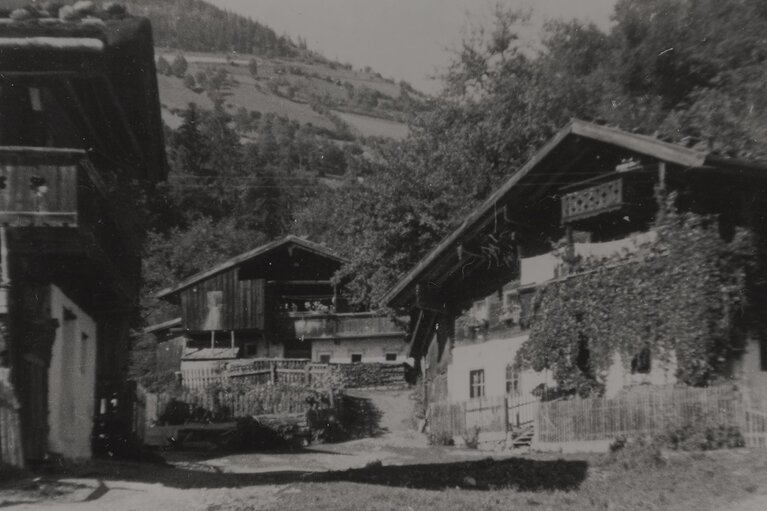 Historische Schwarz-Weiß-Aufnahme mehrerer Bauernhäuser mit Holzaufbauten und Zäunen vor dem Steindorfer Brüggl. | © TVB Piesendorf Niedernsill