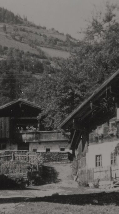 Historische Schwarz-Weiß-Aufnahme mehrerer Bauernhäuser mit Holzaufbauten und Zäunen vor dem Steindorfer Brüggl. | © TVB Piesendorf Niedernsill