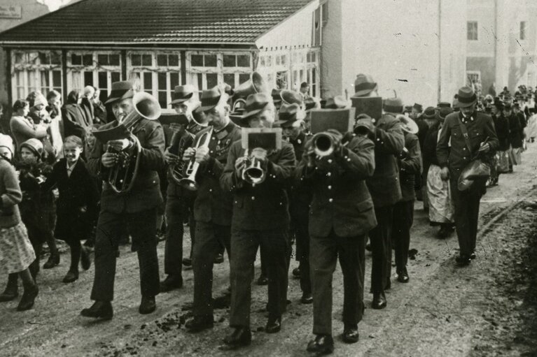Historische Aufnahme der Musikkapelle Piesendorf bei einem Umzug in den 1930er-Jahren, begleitet von Erwachsenen und Kindern. | © TVB Piesendorf Niedernsill