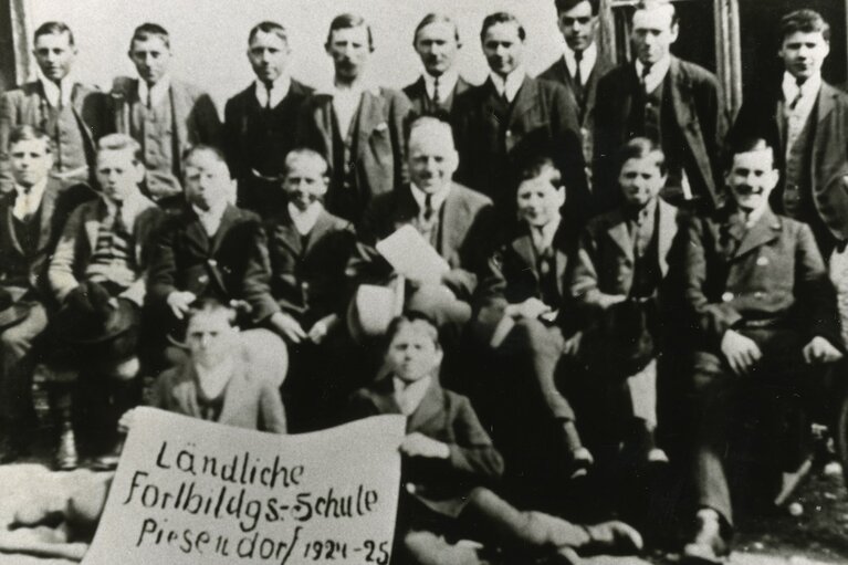Historische Gruppenaufnahme der Ländlichen Fortbildungsschule Piesendorf mit Tafel „1924–25“. | © TVB Piesendorf Niedernsill