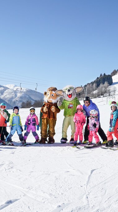Children in ski gear with two animal mascots on the ski slope at Erlebnisberg Naglköpfl in Piesendorf. | © TVB Piesendorf Niedernsill, Foto Harry Liebmann 