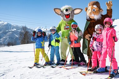 Fünf Kinder auf Ski mit zwei Maskottchen auf einer verschneiten Piste am Erlebnisberg. | © TVB Piesendorf Niedernsill, Foto Harry Liebmann 