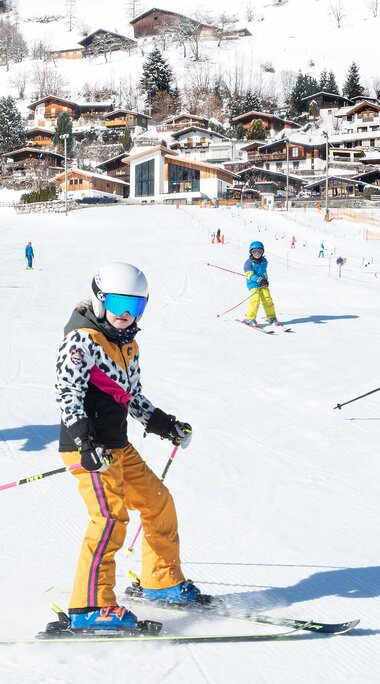 Kinder fahren Ski und Snowboard am Erlebnisberg Naglköpfl in Piesendorf, im Hintergrund liegen Häuser am verschneiten Hang. | © TVB Piesendorf Niedernsill, Foto Harry Liebmann 