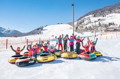 Group of children with colourful snow tubes on a snow-covered area at the Erlebnisberg. | © TVB Piesendorf Niedernsill, Foto Harry Liebmann