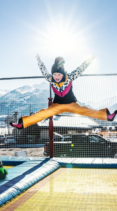 Kinder springen auf einer mit Netzen gesicherten Trampolinanlage am Erlebnisberg Naglköpfl vor verschneiten Bergen. | © TVB Piesendorf Niedernsill, Foto Harry Liebmann
